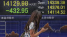 A woman uses a smartphone past an electronic stock board of a securities firm in Tokyo, Friday, July 26, 2013. Japan's Nikkei
