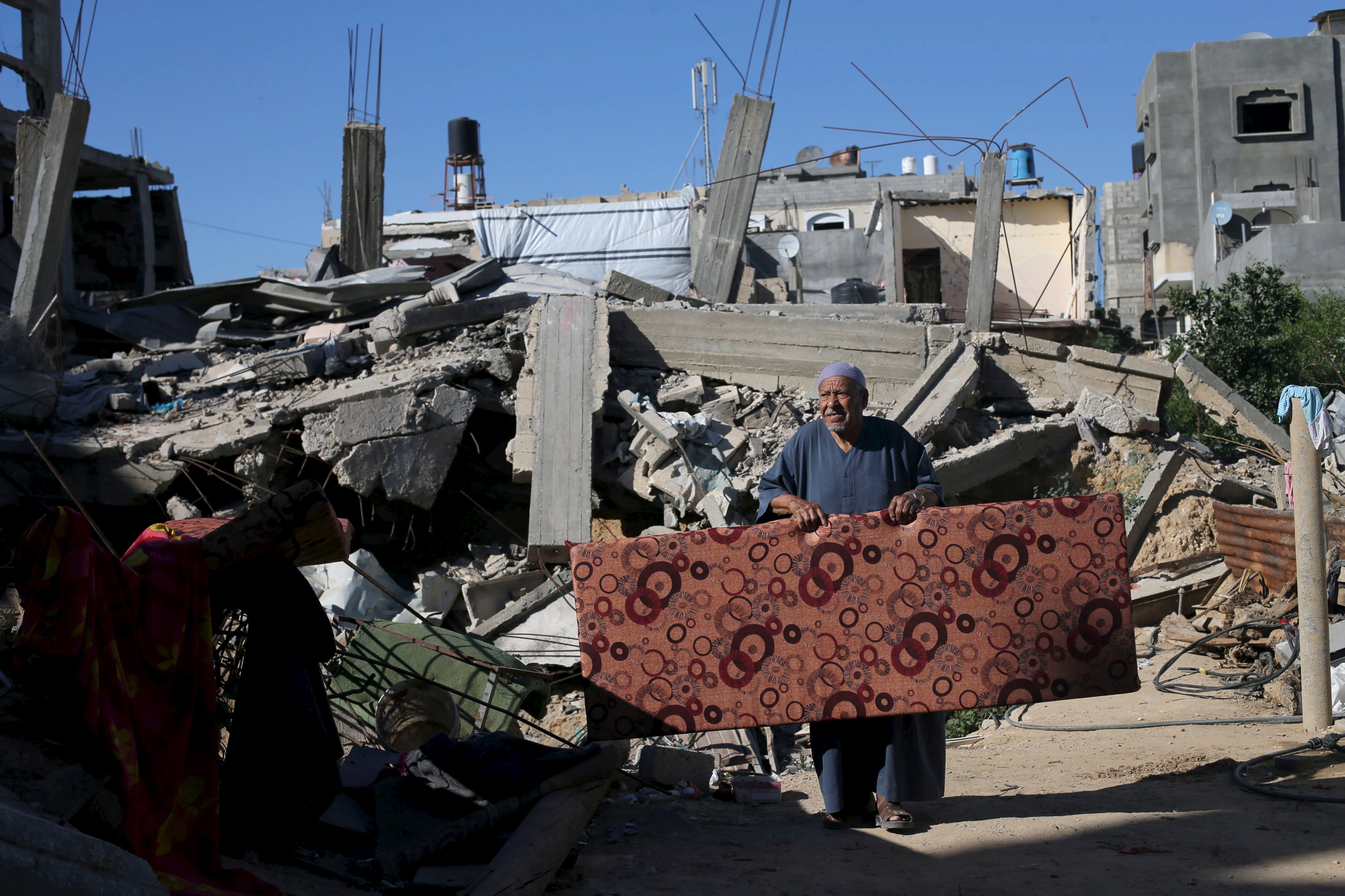 A Palestinian man carries a mattress outside his house that witnesses said was destroyed by Israeli shelling during a 50-day war last summer, in Khan Younis in the southern Gaza Strip June 22, 2015. Israel disputed on Monday the findings of a U.N. report that it may have committed war crimes in the 2014 Gaza conflict, saying its forces acted 