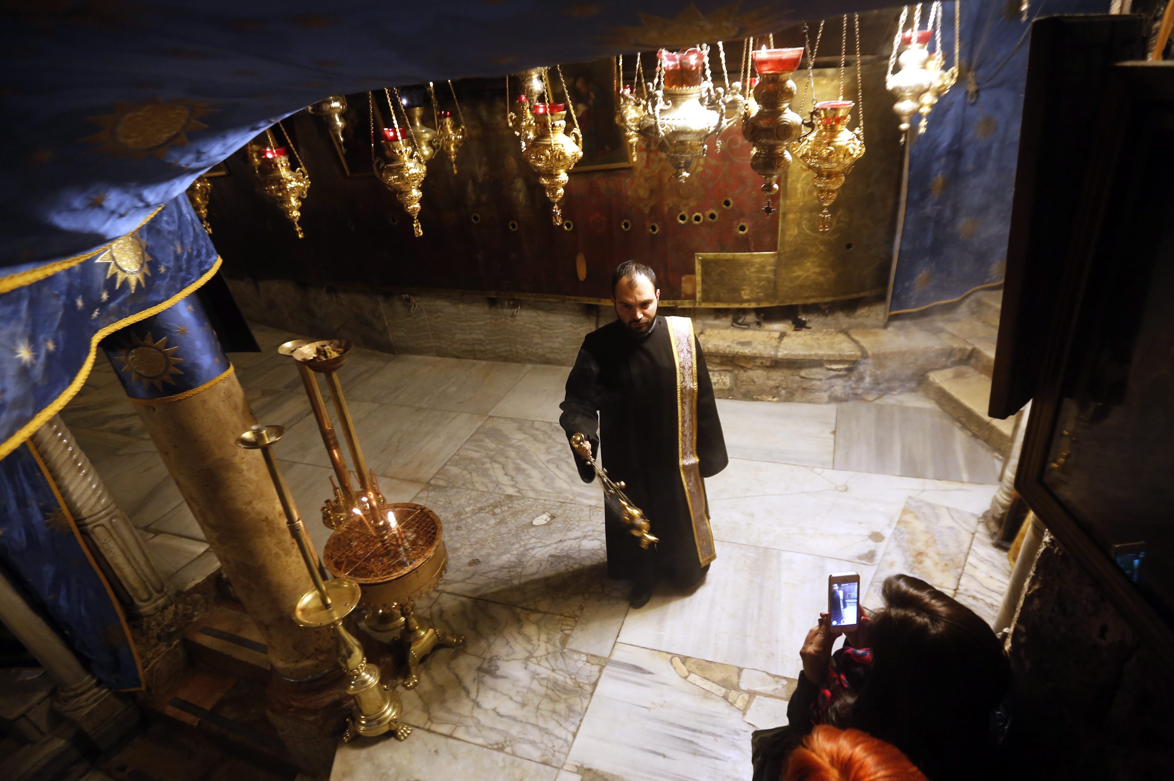 epa05078881 Nuns and pilgrims descend into the 'Grotto' in the Church of the Nativity, the accepted birthplace of Jesus Christ, during a candlelight procession of prayer, in the West Bank city of Bethlehem, 22 December 2015. The church where Jesus was born, one of the world's oldest, is still undergoing massive reconstruction work, and is covered in white plastic sheets and scaffolding. EPA/ABED AL HASHLAMOUN