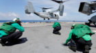 Crewmen brace themselves from the propeller wash of a Marine Corps MV-22B Osprey departing the aboard the USS Kearsarge as U.