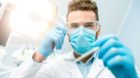 Portrait of scary dentist in mask and protective eyeglasses with dental tools during the surgery looking at camera