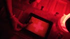 Darkroom printing process photographer using enlarger to produce photographic prints.Woman working in a red dark room.